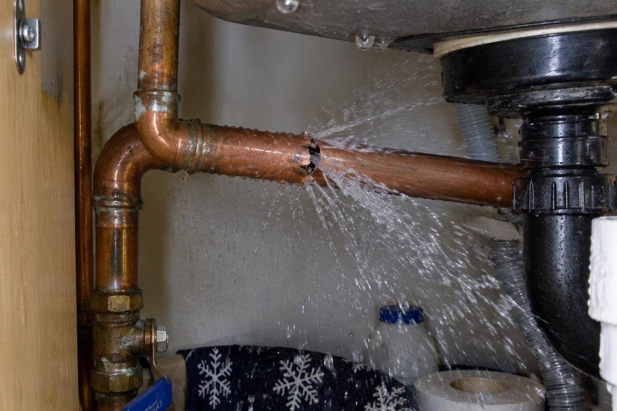 Burst copper pipe spraying water under a kitchen sink during winter